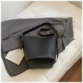 Detail of minimalist black bucket bag with lychee grain texture on gray blazer - Black