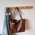 Detail of vintage brown tote bag hanging on wooden hook with denim jacket background - Brown with Pendant