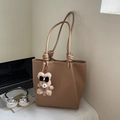 Brown leather tote bag with knot strap detail and bear charm in a desk setting - Khaki With Pendant