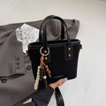 Detalle de bolso negro acolchado con tachuelas doradas y amuleto de madera sobre traje gris - Negro
