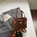 Bolso cubo de ante marrón con herrajes dorados y adorno de felpa sobre cama blanca - Marrón
