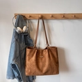 Caramel brown woven tote bag with suede texture and metallic detail hanging on a rack - Brown No Pendant