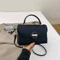 Detail of black pebbled leather handbag featuring a golden round metal twist lock - Black