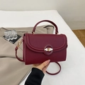 Detail of burgundy lychee pattern leather handbag with gold metal clasp and stitching - Burgundy