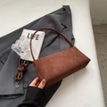 Detailaufnahme der braunen Wildleder-Baguette-Tasche auf grauem Anzug mit Buchstütze - Braun