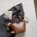 Dunkelbraune matte Handtasche mit Knotengriffen und Bärenanhänger auf einem Anzug - Gelbbraun mit Anhänger