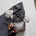 Dunkelbraune minimalistische Lederhandtasche mit Bärenanhänger auf grauem Blazer - Kaffee mit Anhänger