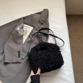Close-up of black plush faux fur shoulder bag with leather strap on white bedding - Black