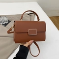 Close-up of brown litchi pattern leather handbag with gold metal clasp detail - Brown