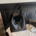 Detalle del bolso grande de hombro en cuero negro con hebilla dorada sobre cama - Negro