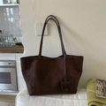 Detalle del bolso tote de cuero mate marrón oscuro con asas largas sobre un sofá - Marrón