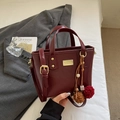 Elegante bolso tipo cubo en cuero sintético granate con herrajes dorados y pompón decorativo - Rojo Vino Con Colgante