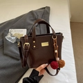 Bolso tipo cubo marrón oscuro en cuero sintético brillante con herrajes dorados y pompón - Café con Colgante