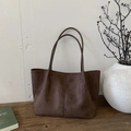 Detalle de un bolso tote de ante marrón oscuro con costura vertical en una mesa de madera mínima - Marrón
