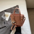 Dettaglio della borsa a secchiello rosa in pelle sintetica opaca con ciondolo grigio - rosa con ciondolo