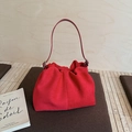 Dettaglio di una borsa in camoscio rosso con pieghe morbide su un cuscino marrone - Rosso