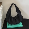 Dettaglio della borsa a mezzaluna in camoscio nero minimalista su un libro di design - Nero