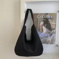 Detail of a black suede hobo bag with a wide strap hanging against a minimalist wall - Black
