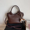 Detail einer dunkelbraunen geflochtenen Handtasche mit Henkel und Plüschwelpen-Anhänger - Mit Anhänger / Braun