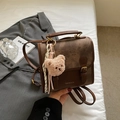 Detalle de mochila vintage marrón con logo de moda, colgante de oso y tela texturizada - Marrón