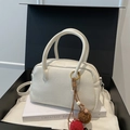 Weiße Boston Bag mit Lederstruktur und Plüsch-Anhänger auf einer Geschenkbox - Cremeweiß mit Anhänger