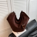 Macro detail of brown suede tote bag featuring a curved opening and metal charm - Brown