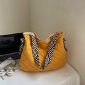 Close-up of yellow quilted tote bag with black and white striped handles and bows - Yellow