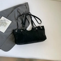 Dettaglio della borsa tote scamosciata nera con occhielli d'argento su un blazer grigio - Nero
