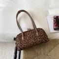 Dettaglio della borsa Boston leopardata con manici in pelle su una panca intrecciata - Marrone