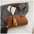 Detail einer braunen matten Bowlingtasche mit Perlenanhängern auf grauem Anzugshintergrund - Braun mit Anhänger