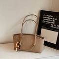 Dettaglio di una borsa tote beige con marchio in rilievo e ciondolo in legno a perline - Cachi