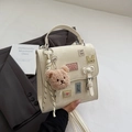 Gros plan du sac en cuir PU crème avec des patchs brodés et un porte-clé ours en peluche marron - Blanc Cassé