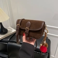 Détail d'un sac bandoulière rétro en daim marron avec breloques et boucle dorée élégante - Café Avec Pendentif