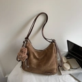 Brown hobo shoulder bag with a teddy bear charm shown next to a laptop on a white desk - Brown with Pendant
