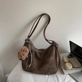 Detail van vintage bruine leren tas met teddybeer-bedel en zilveren merkplaatje erop - Koffie Met Bedels