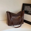 Grande borsa tote marrone scuro con rivetti e tasca con zip su uno sfondo minimalista - caffè