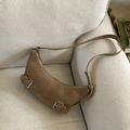 Detail of a brown suede crescent bag with silver buckle on a cozy beige sofa - Khaki