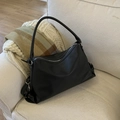 Detalle de bolso de hombro de cuero negro con textura de lichi sobre un sofá acogedor - Negro