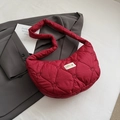 Detail of red heart-quilted dumpling bag featuring a wide shoulder strap and woven label - Red