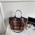Detail of a brown leather and plaid tote bag with dual handles on a white desk - Brown Grid