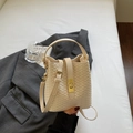 Schicke beige gewebte Eimertasche mit Goldschließe auf grauem Sakko-Hintergrund - Cremeweiß