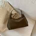 Dettaglio di una borsa sottobraccio in camoscio marrone su un divano beige con maglia - Verde