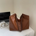 Detail einer braunen PU-Tasche mit Vintage-Kette und Logo auf einem modernen Schreibtisch - Braun