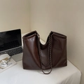 Detail der weichen dunkelbraunen Leder-Tote-Bag mit bronzefarbener Kette auf weißem Tisch - Kaffeebraun