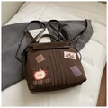 Détail du sac à dos vintage marron foncé avec des écussons créatifs sur une parure de lit blanche - Sans Pendentif / Marron