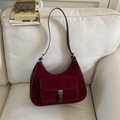 Detail of burgundy suede shoulder bag with brown leather strap on a soft white sofa - Red
