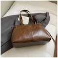 Nahaufnahme der braunen Retro-Ledertasche mit Silberlogo und seitlichem Kordelzug - Braun
