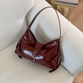 Close-up of glossy deep red patent leather bag with silver metal hook on a white sofa - Red