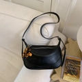 Detalle de bolso hobo negro con colgante de cuentas de madera en un sofá beige texturizado - Negro con colgante