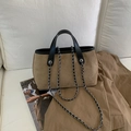 Dettaglio borsa shopper in camoscio marrone con manici in pelle nera su divano bianco - Cachi